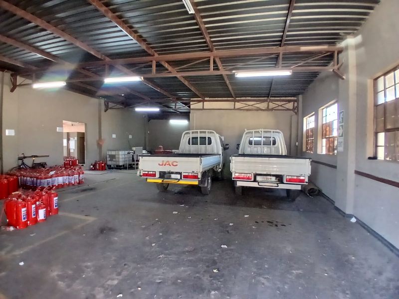 Spacious industrial garage or warehouse area featuring exposed steel roof trusses, concrete flooring, and ample natural light through multi-pane windows.