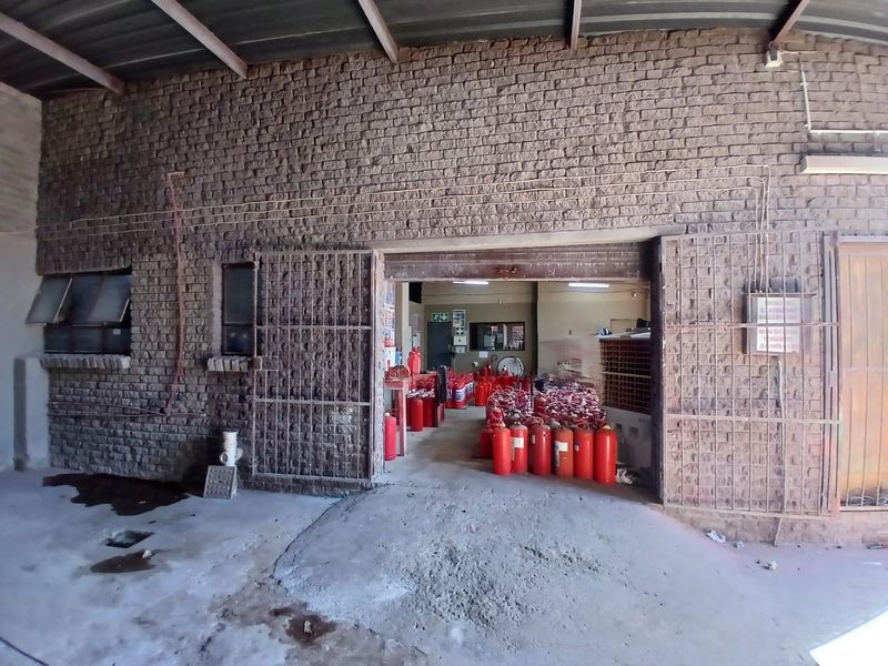 Industrial utility space featuring exposed brick walls, concrete flooring, and a large sliding metal security gate, currently utilized for storage.