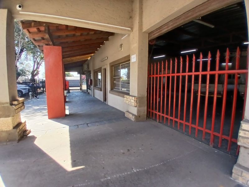Industrial exterior front featuring a covered walkway, concrete flooring, and a secure gated entrance to the workshop area.