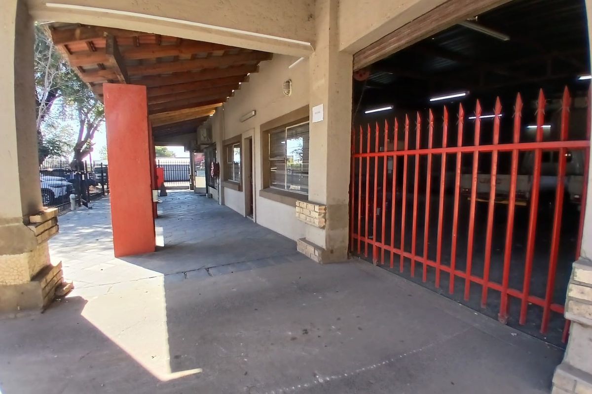 Industrial exterior front featuring a covered walkway, concrete flooring, and a secure gated entrance to the workshop area.