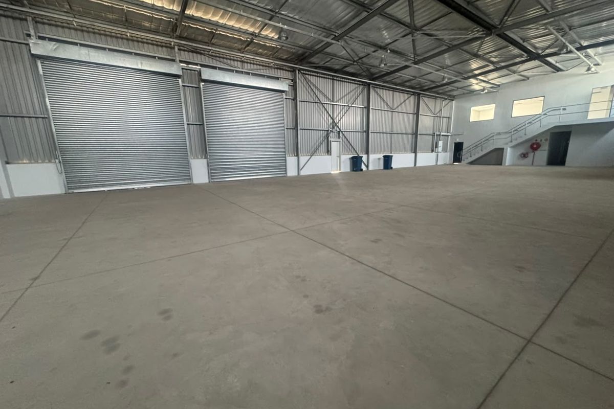Spacious industrial warehouse featuring high ceilings with exposed steel trusses, concrete flooring, and multiple large roller shutter doors for easy access.