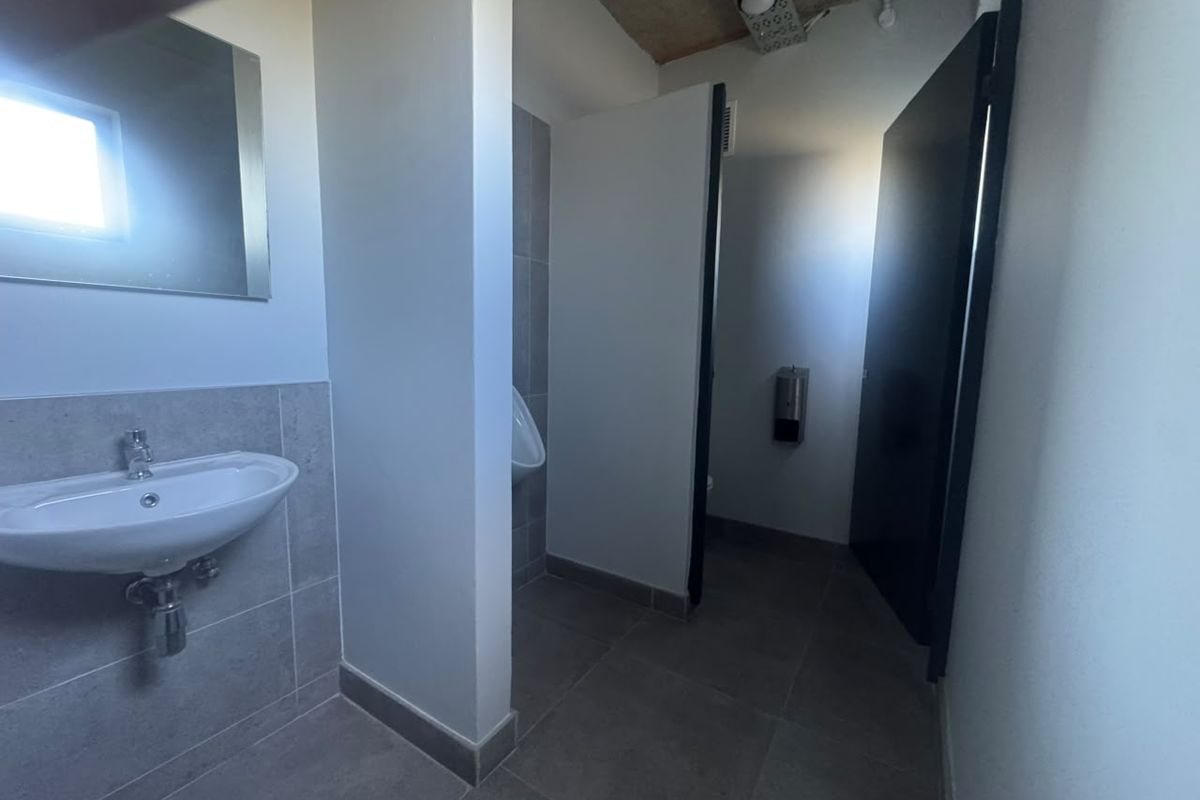 A clean, modern industrial-style bathroom featuring a wall-mounted basin, tiled flooring, and a private urinal stall.