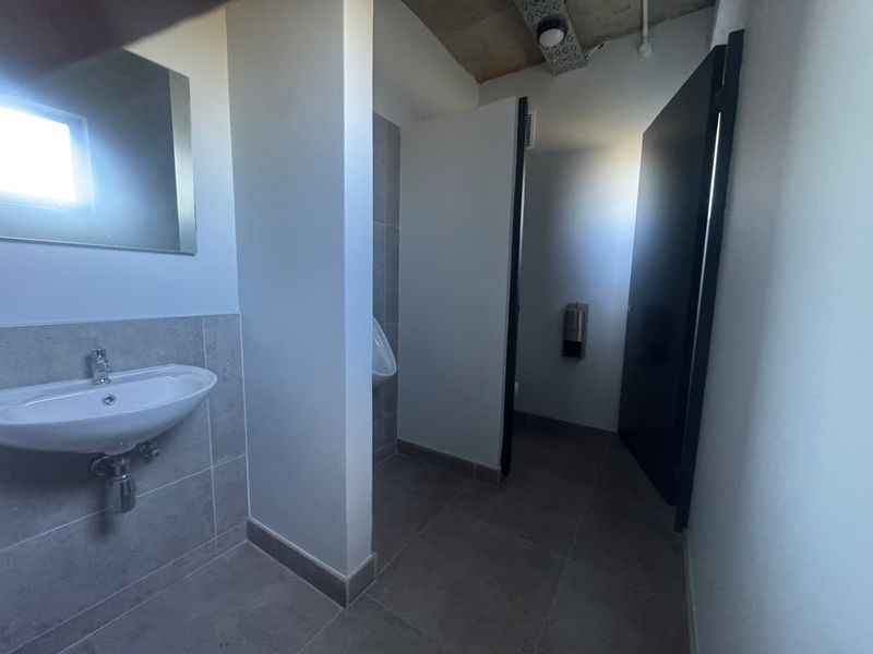 A clean, modern industrial-style bathroom featuring a wall-mounted basin, tiled flooring, and a private urinal stall.