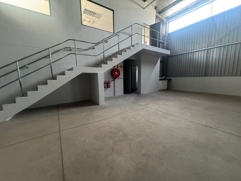 Spacious industrial utility area featuring a concrete staircase with metal handrails, high-level windows, and durable concrete flooring.