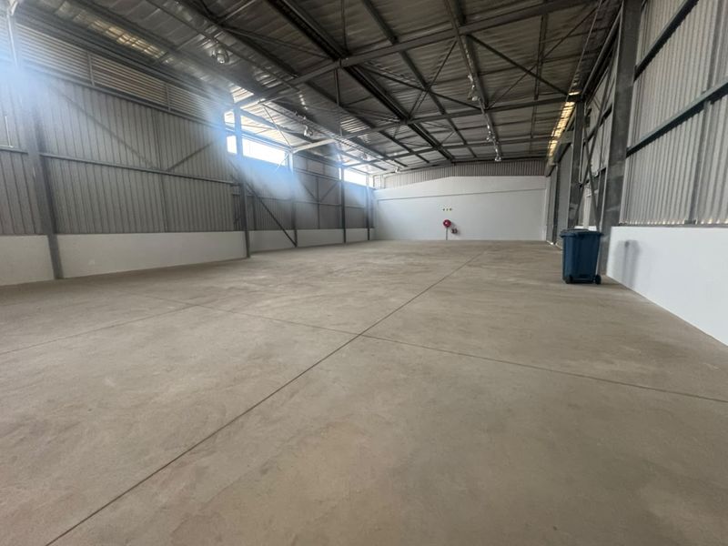 Spacious industrial warehouse unit featuring high ceilings with exposed steel trusses, durable concrete flooring, and corrugated metal wall cladding.