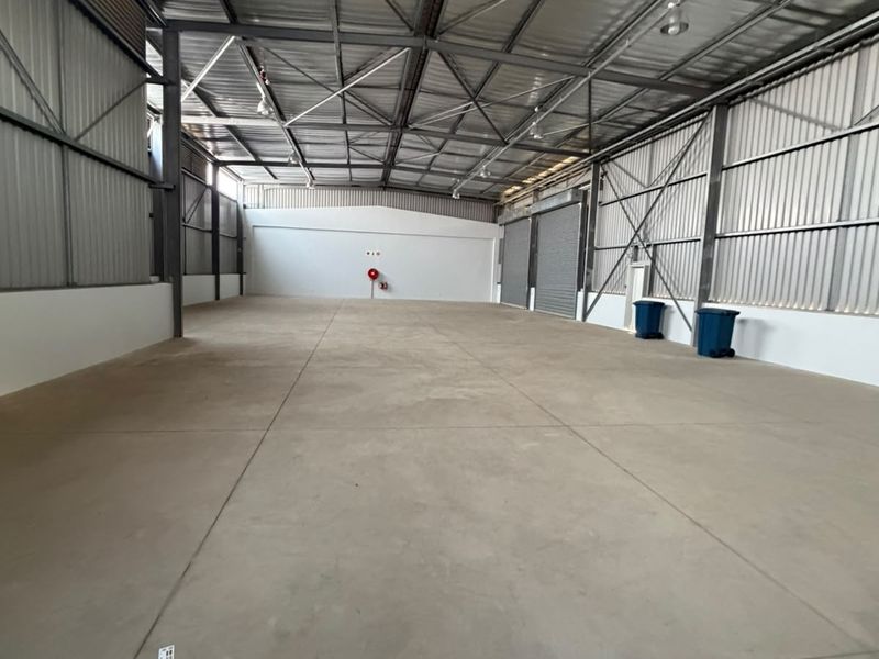 Spacious industrial warehouse unit featuring high ceilings with exposed steel trusses, concrete flooring, and large roller shutter doors for easy access.