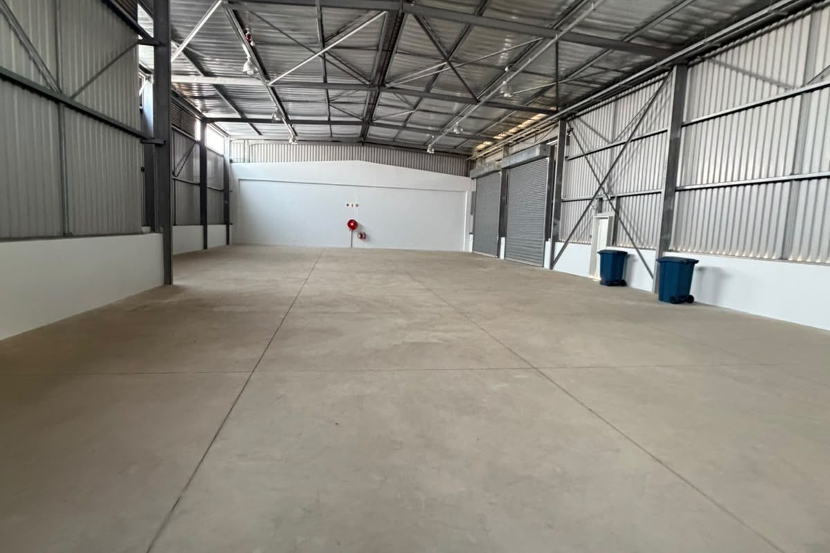 Spacious industrial warehouse unit featuring high ceilings with exposed steel trusses, concrete flooring, and large roller shutter doors for easy access.