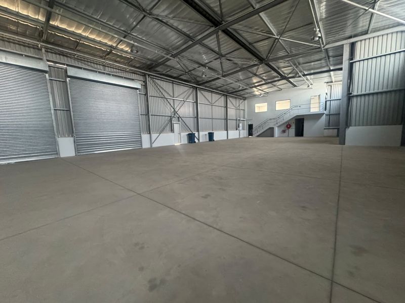 Spacious industrial warehouse featuring high ceilings, concrete flooring, large roller shutter doors, and a mezzanine level with staircase access.