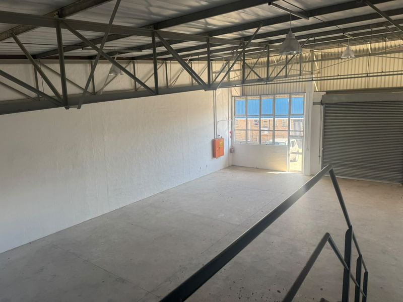 Spacious industrial utility area featuring exposed steel roof trusses, concrete flooring, a roller shutter door, and functional industrial lighting.