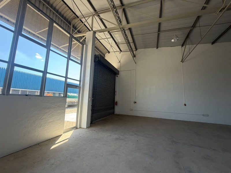 Spacious industrial utility area featuring high ceilings with exposed steel trusses, concrete flooring, and a large roller shutter door for easy access.