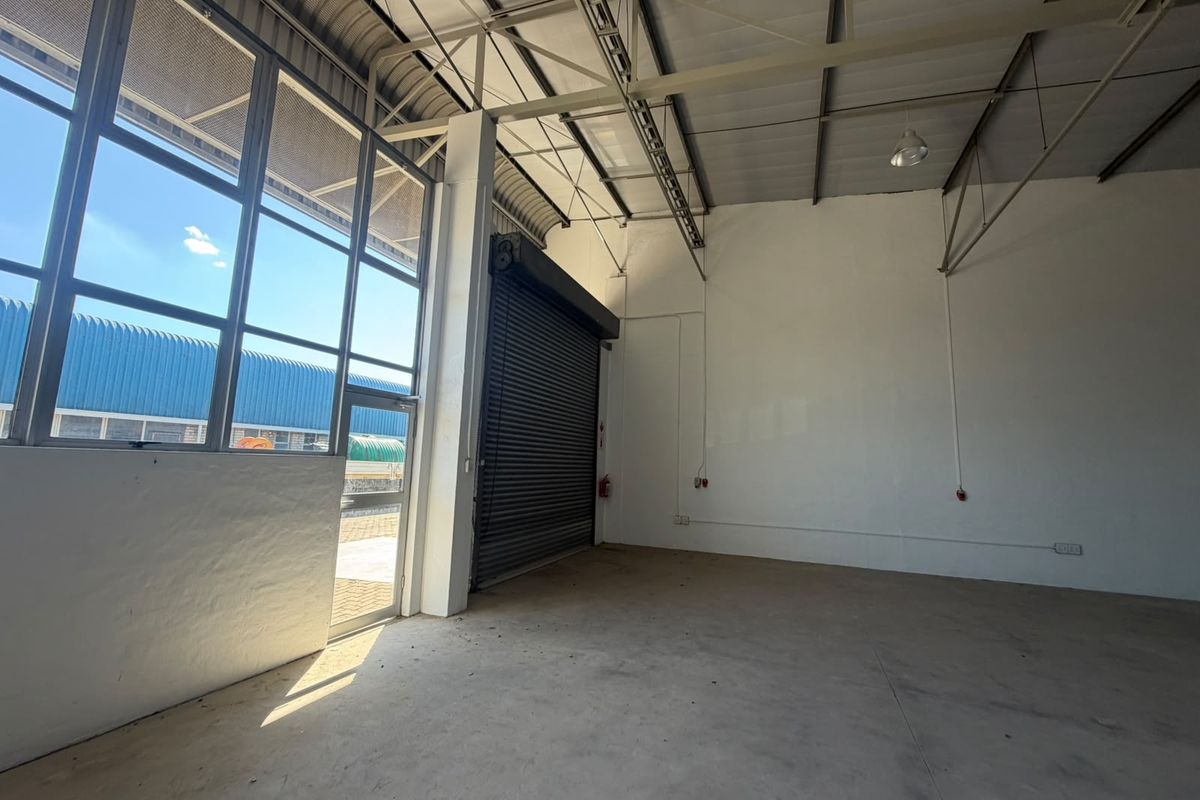 Spacious industrial utility area featuring high ceilings with exposed steel trusses, concrete flooring, and a large roller shutter door for easy access.