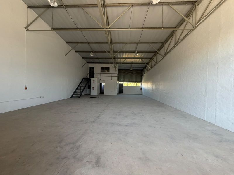 Spacious industrial warehouse unit featuring high ceilings with exposed steel trusses, concrete flooring, and a mezzanine level with an integrated staircase.