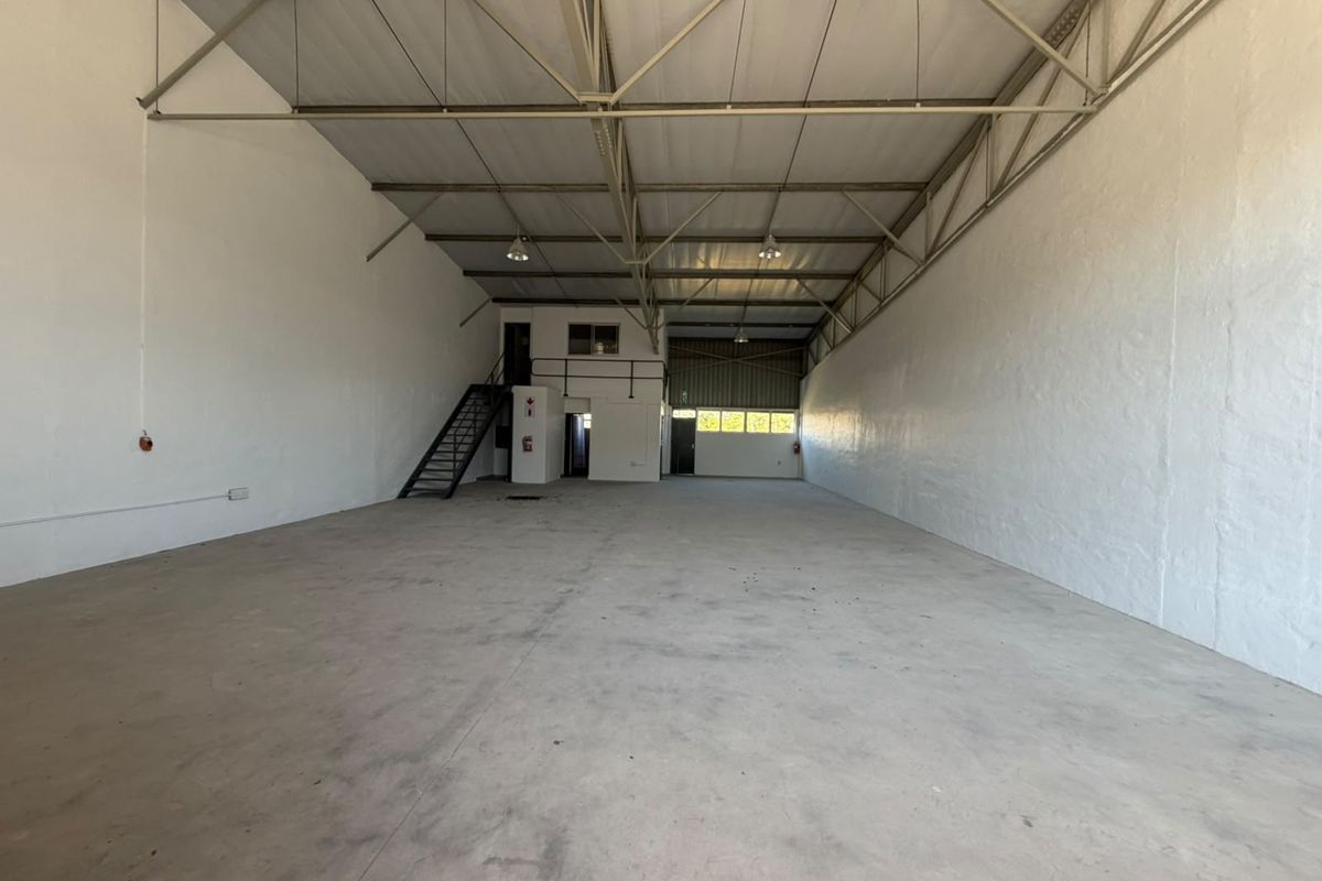 Spacious industrial warehouse unit featuring high ceilings with exposed steel trusses, concrete flooring, and a mezzanine level with an integrated staircase.