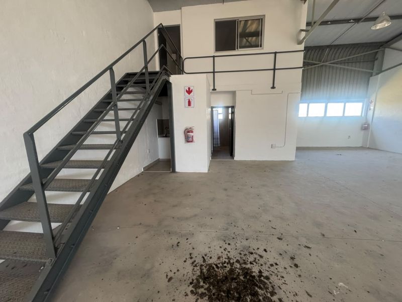Open-plan industrial utility space featuring a metal staircase leading to a mezzanine level, concrete flooring, and integrated fire safety equipment.