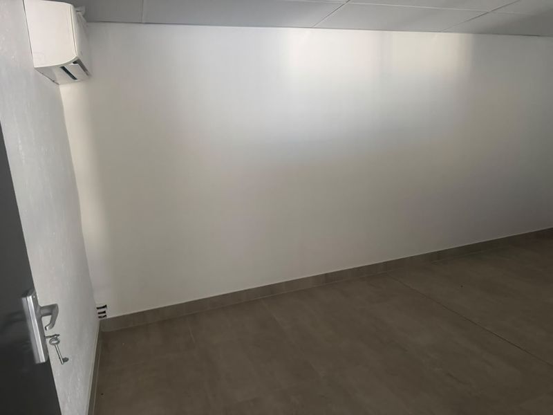 A clean, empty office space featuring tiled flooring, a suspended ceiling, and a wall-mounted split-system air conditioning unit.