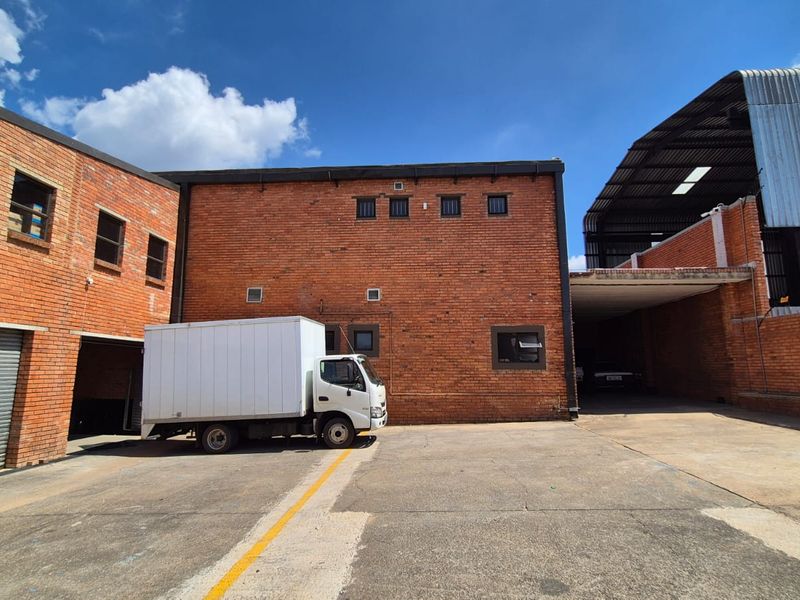 Rear industrial yard featuring exposed brick facade, roller shutter door access, and a covered loading bay area with concrete hardstand.