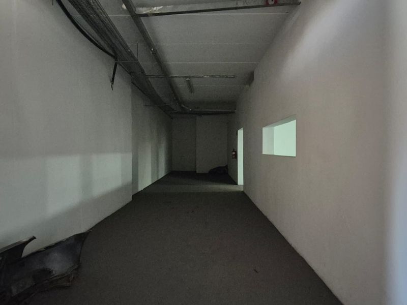 An empty industrial utility space featuring exposed cable trays, plain walls, and a fire extinguisher, suitable for storage or workshop use.
