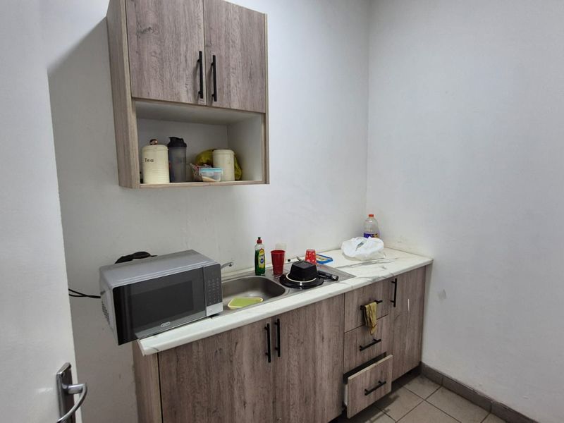 A compact scullery area featuring wood-look built-in cabinetry, a stainless steel sink, and durable tiled flooring, providing functional utility space.