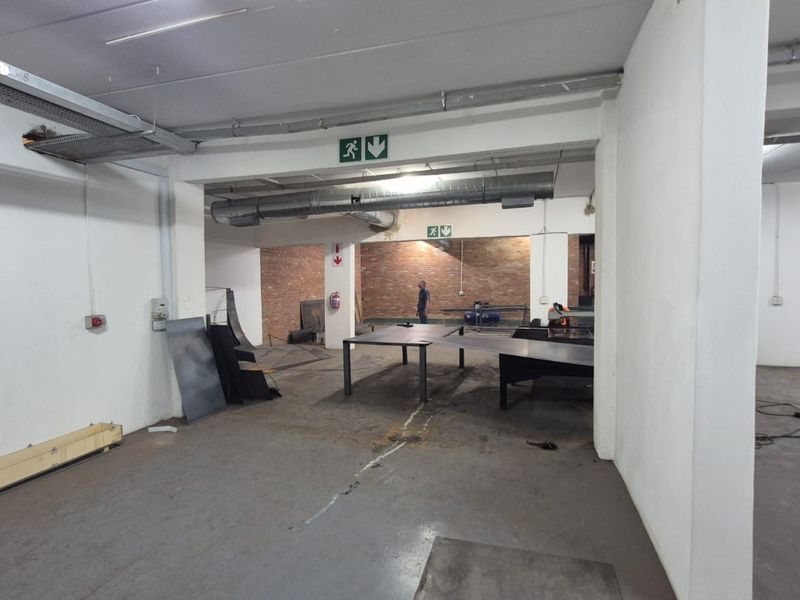 An open-plan industrial utility space featuring exposed brickwork, concrete flooring, and overhead ducting, suitable for workshop or storage use.