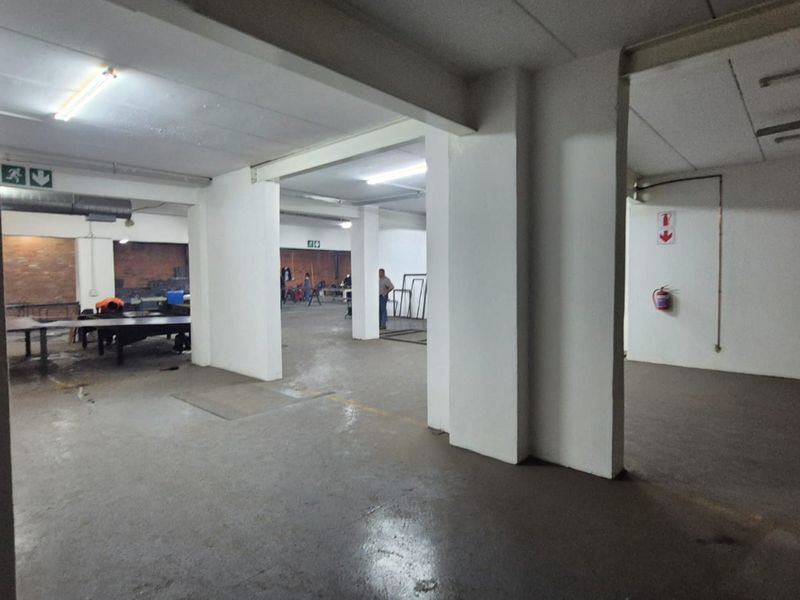 Spacious industrial utility area featuring concrete flooring, exposed ducting, and functional fluorescent lighting, suitable for workshop or storage operations.