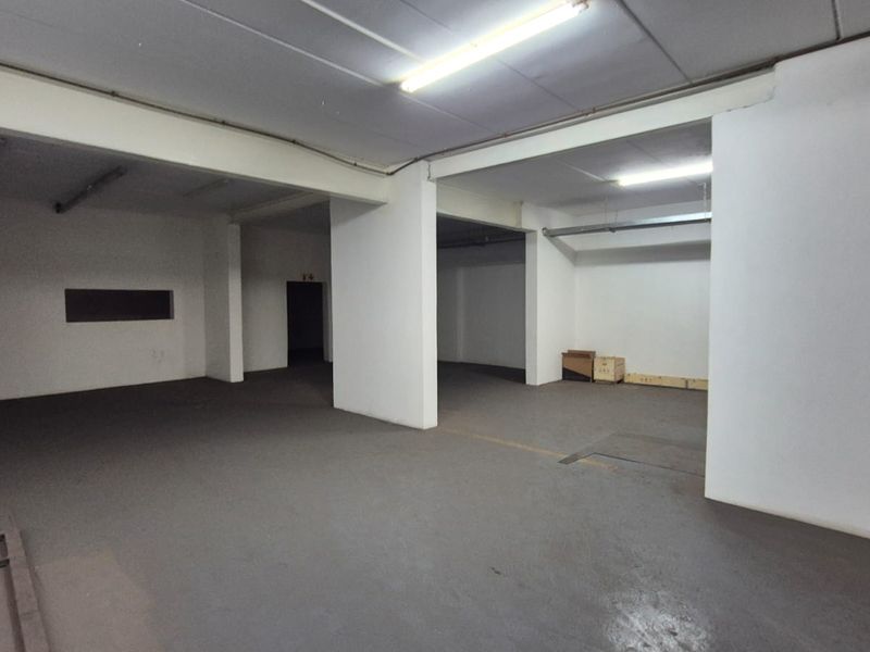 A spacious, open-plan industrial utility area featuring concrete flooring, support columns, and overhead fluorescent lighting, suitable for storage or workshop use.