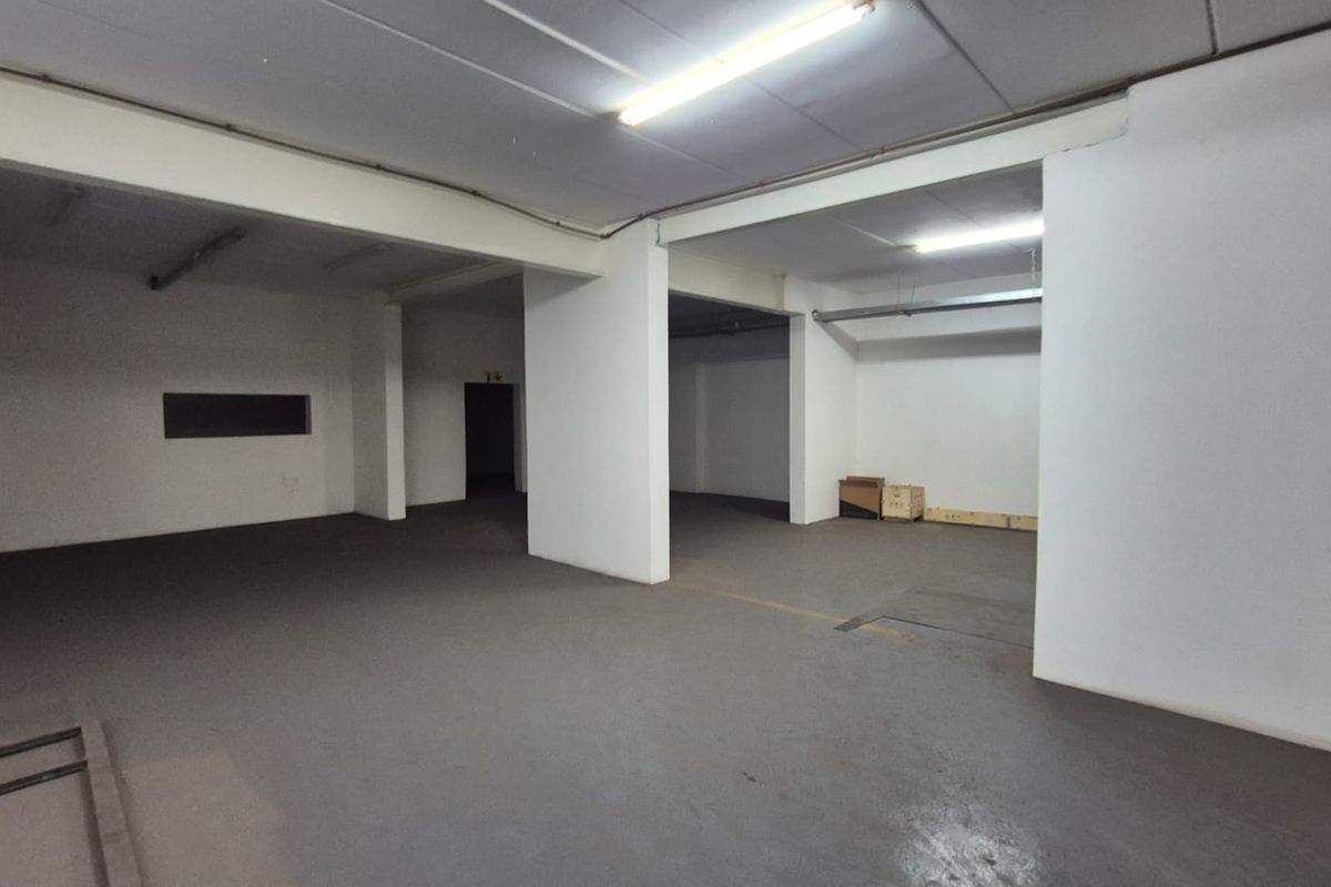 A spacious, open-plan industrial utility area featuring concrete flooring, support columns, and overhead fluorescent lighting, suitable for storage or workshop use.