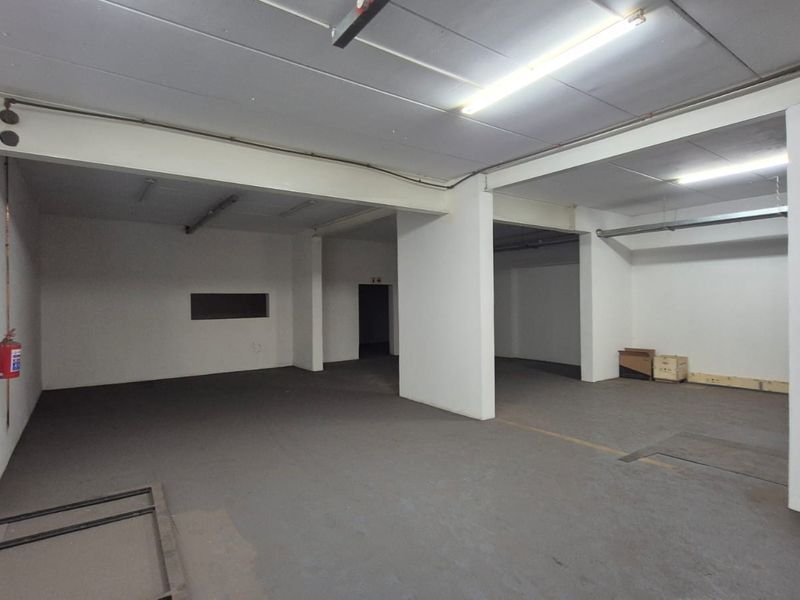 A spacious, open-plan industrial utility area featuring concrete flooring, exposed structural beams, and functional overhead fluorescent lighting.