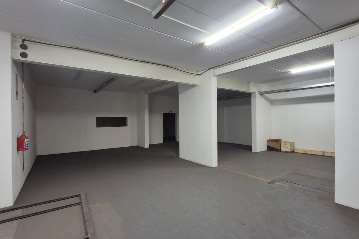 A spacious, open-plan industrial utility area featuring concrete flooring, exposed structural beams, and functional overhead fluorescent lighting.