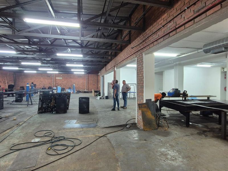 Spacious industrial workshop area featuring exposed brick walls, steel roof trusses, and concrete flooring, suitable for manufacturing or storage operations.
