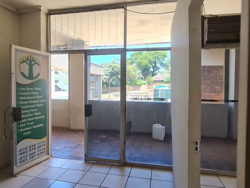 An empty office space featuring tiled flooring, aluminium framed glass partitions, and a wall-mounted air conditioning unit, offering a functional layout for business use.