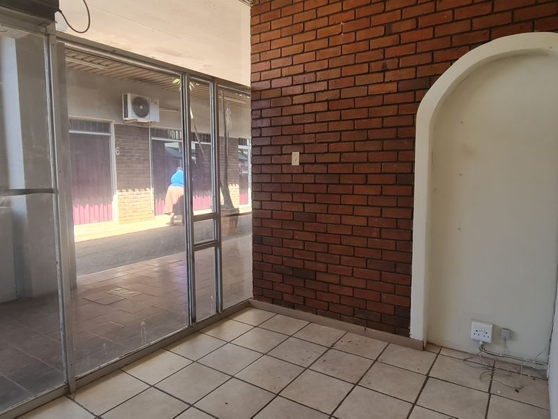 Empty office space featuring an exposed brick feature wall, arched wall niche, tiled flooring, and large aluminum-framed glass partitions.