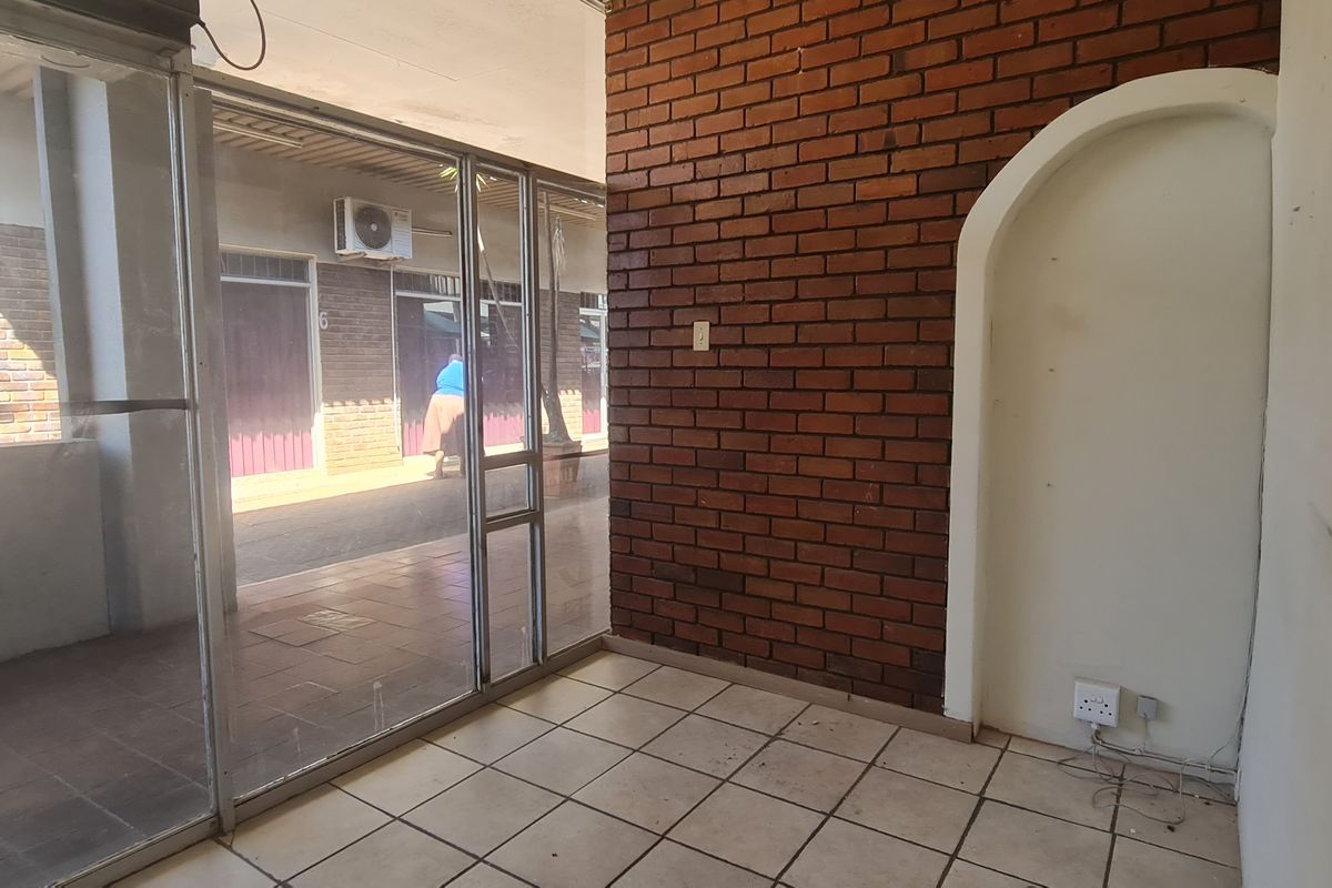 Empty office space featuring an exposed brick feature wall, arched wall niche, tiled flooring, and large aluminum-framed glass partitions.