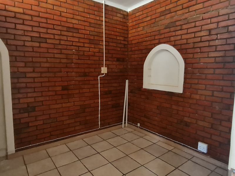 An empty office space featuring exposed brick walls, tiled flooring, and a decorative arched wall niche.