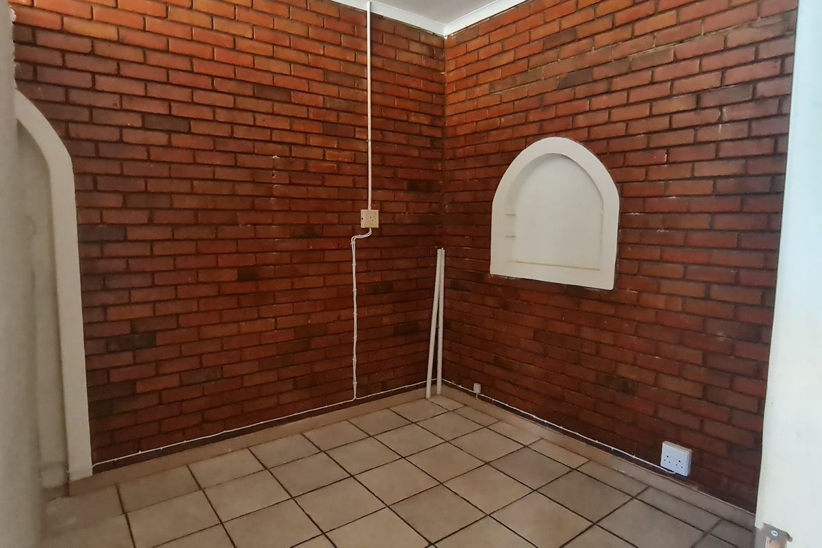 An empty office space featuring exposed brick walls, tiled flooring, and a decorative arched wall niche.