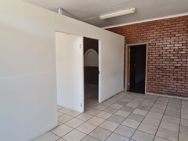 An empty office space featuring exposed brickwork, tiled flooring, and a partition wall, offering a blank canvas for professional customization.