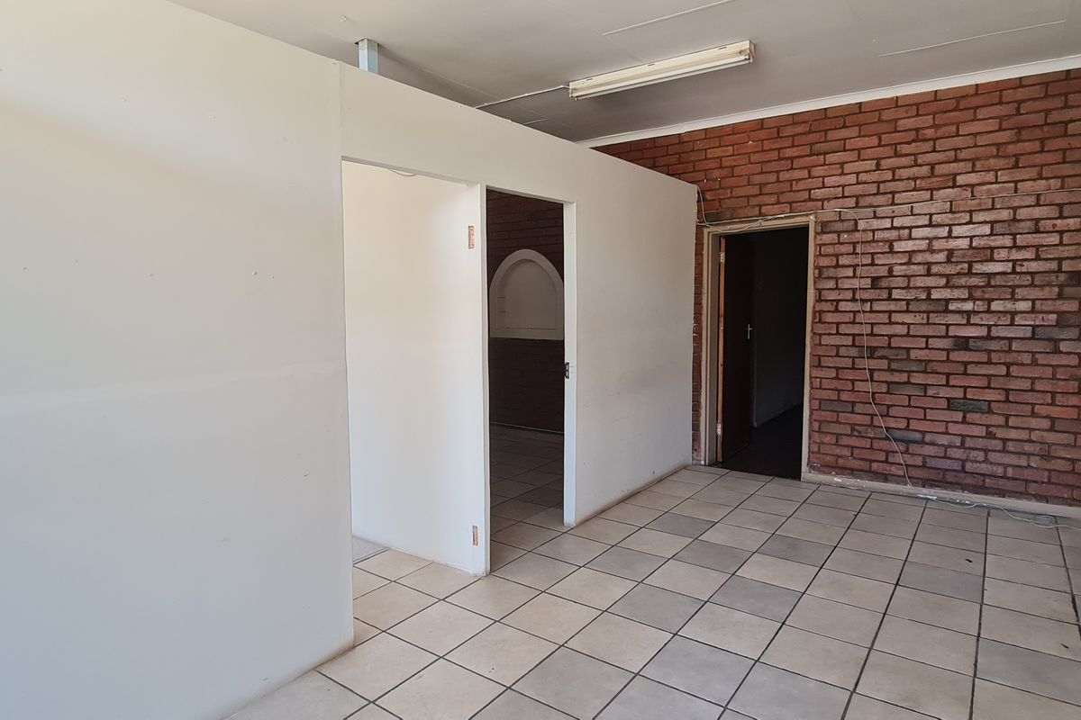 An empty office space featuring exposed brickwork, tiled flooring, and a partition wall, offering a blank canvas for professional customization.