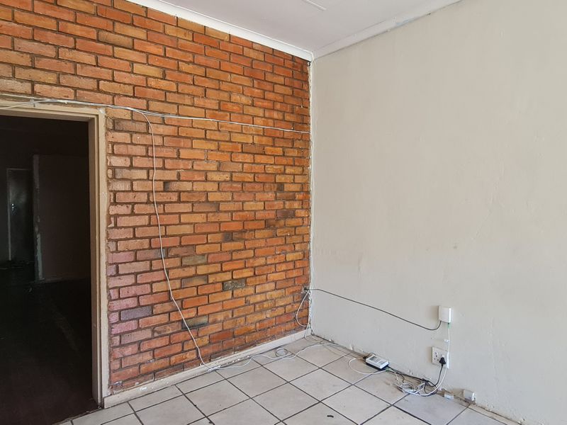 An empty office space featuring an exposed brick wall, ceramic tiled flooring, and visible surface wiring.