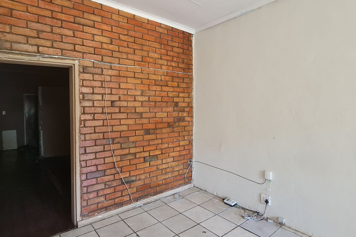 An empty office space featuring an exposed brick wall, ceramic tiled flooring, and visible surface wiring.