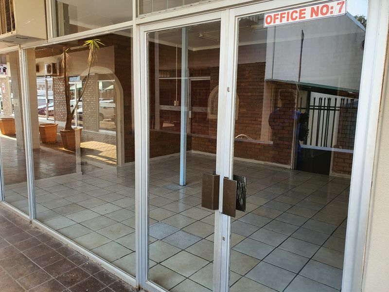 A vacant office space featuring a glass storefront, tiled flooring, and exposed brick walls, suitable for a professional workspace.