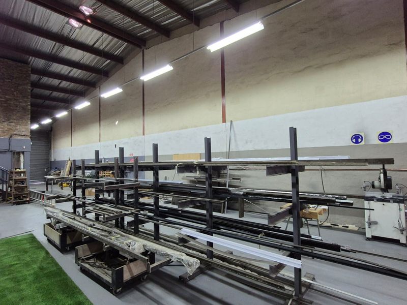 Spacious industrial utility area featuring high ceilings with exposed steel trusses, durable concrete flooring, and extensive built-in metal racking for storage.