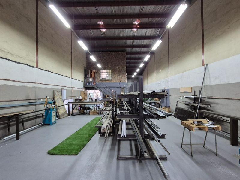 Spacious industrial utility space featuring high ceilings with exposed steel trusses, fluorescent lighting, concrete flooring, and a mezzanine level with brick accents.
