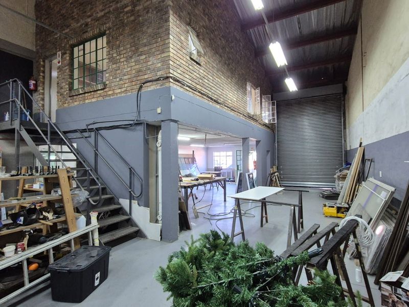 Spacious industrial utility area featuring exposed brickwork, a mezzanine level, steel staircase, and a large roller shutter door for easy access.