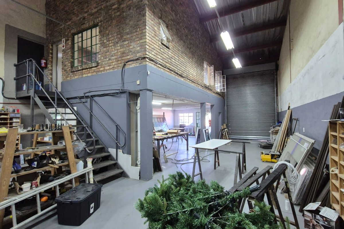 Spacious industrial utility area featuring exposed brickwork, a mezzanine level, steel staircase, and a large roller shutter door for easy access.
