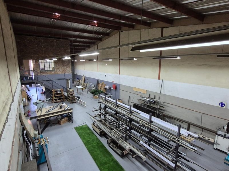 Spacious industrial warehouse unit featuring high ceilings with exposed steel trusses, concrete flooring, mezzanine level, and functional industrial lighting throughout.