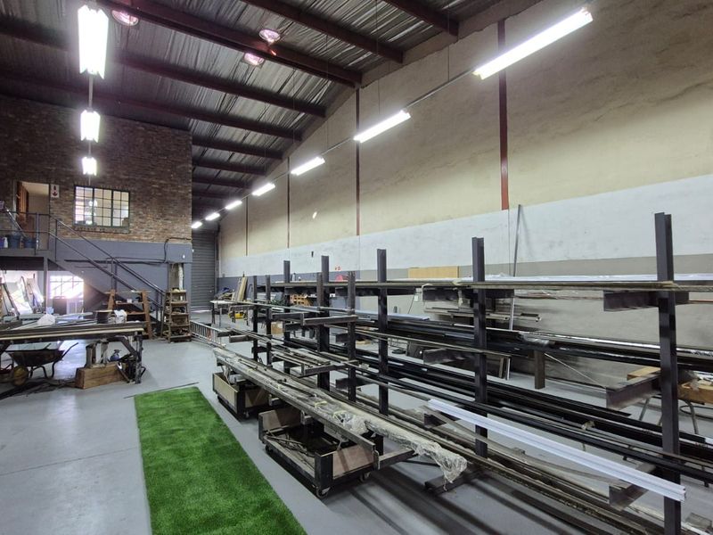 Spacious industrial warehouse unit featuring high ceilings with exposed steel trusses, concrete flooring, mezzanine level, and integrated industrial storage racking.