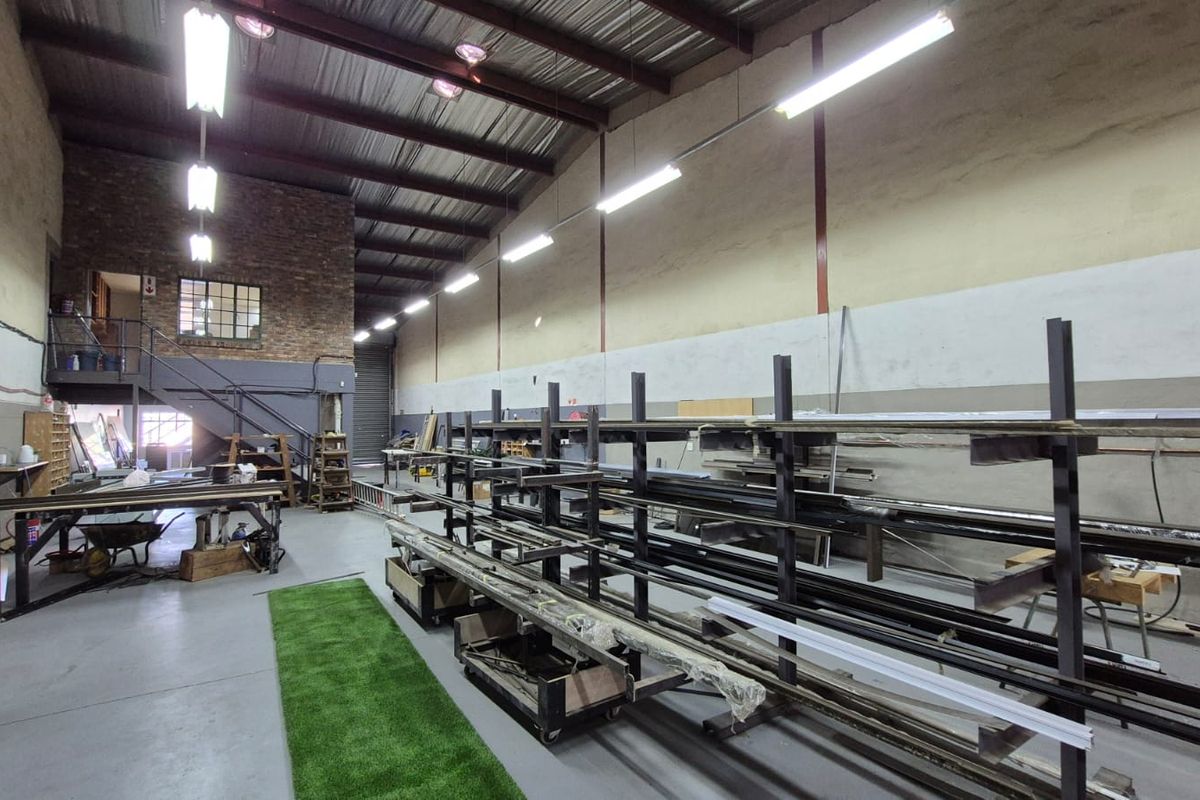 Spacious industrial warehouse unit featuring high ceilings with exposed steel trusses, concrete flooring, mezzanine level, and integrated industrial storage racking.