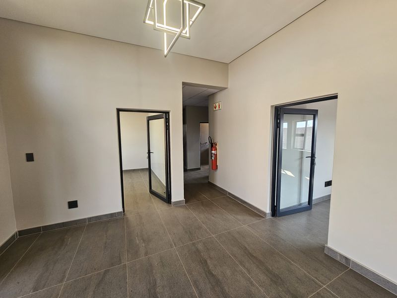 A clean, modern industrial hallway featuring tiled flooring, contemporary lighting, and multiple glass-paneled doorways leading to adjacent office or utility spaces.
