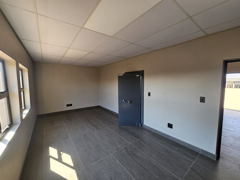 A clean, empty office space featuring modern tiled flooring, a drop ceiling, and a secure built-in safe.