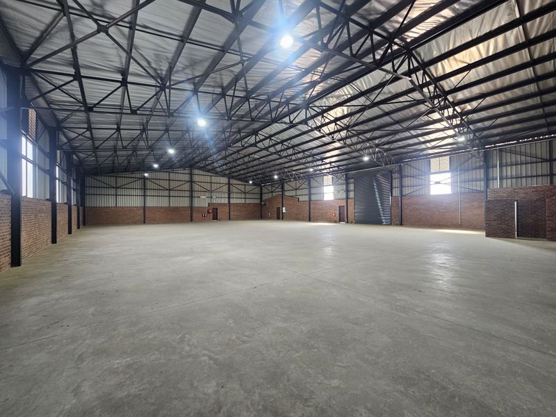 Spacious industrial warehouse featuring high-clearance exposed steel truss roofing, polished concrete floors, exposed brick walls, and a large roller shutter door.