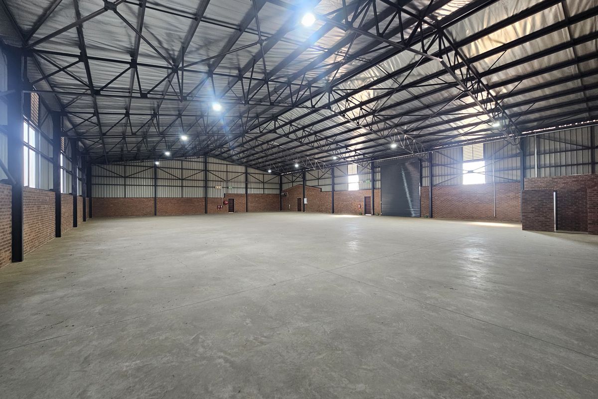 Spacious industrial warehouse featuring high-clearance exposed steel truss roofing, polished concrete floors, exposed brick walls, and a large roller shutter door.